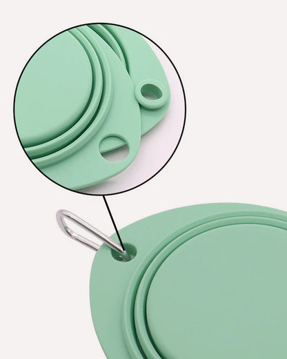 Close-up of the cyan collapsible travel double dog bowl, emphasizing the convenient carabiner attachment and the dual hole design for easy portability and secure hanging.