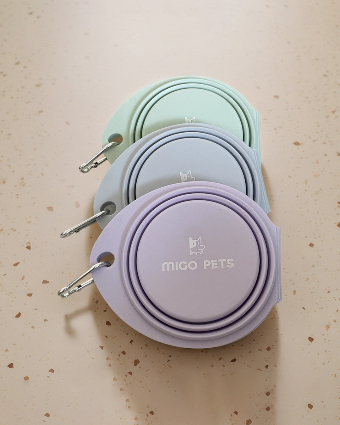 Three folded collapsible travel double dog bowls in pastel colors, stacked neatly.