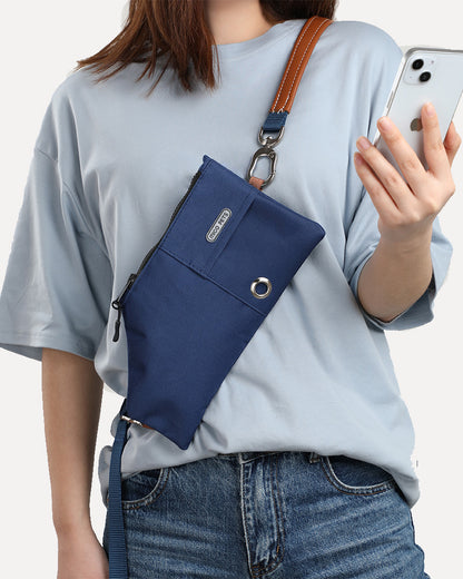 A person wearing a navy-blue crossbody travel pouch, freeing her hands to use her phone.
