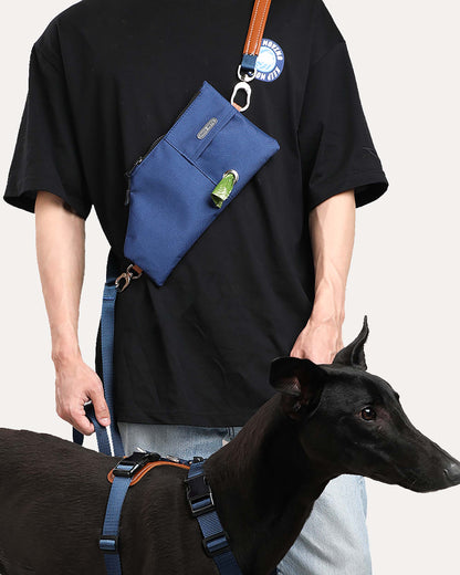 A person walking a dog while wearing a navy blue durable and versatile crossbody travel pouch.