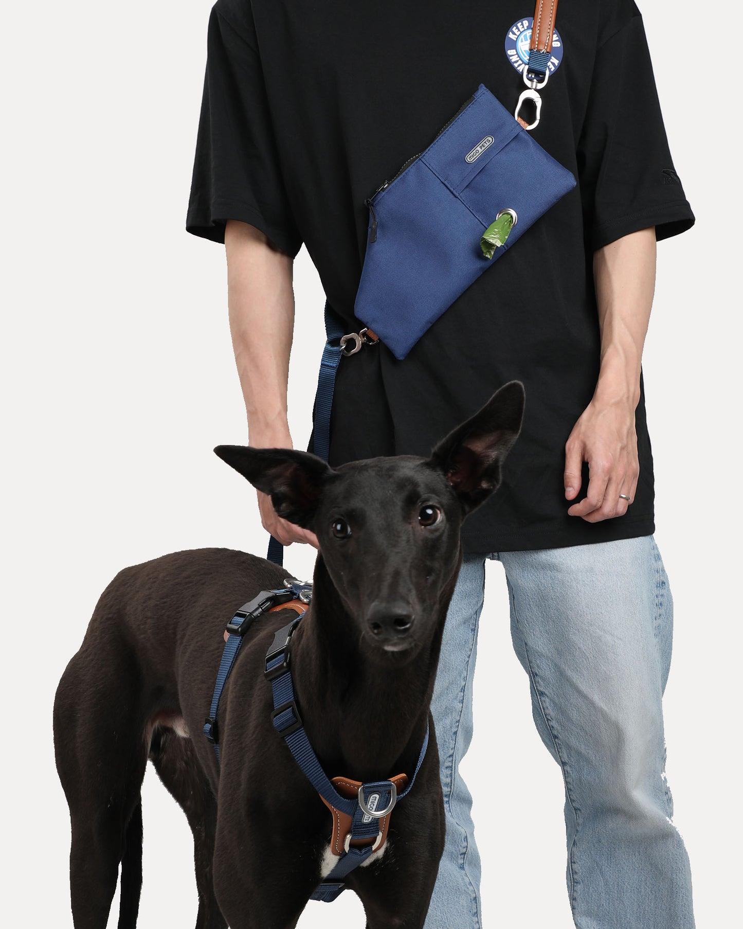 A person walking a dog while wearing a navy blue durable and versatile crossbody travel pouch.