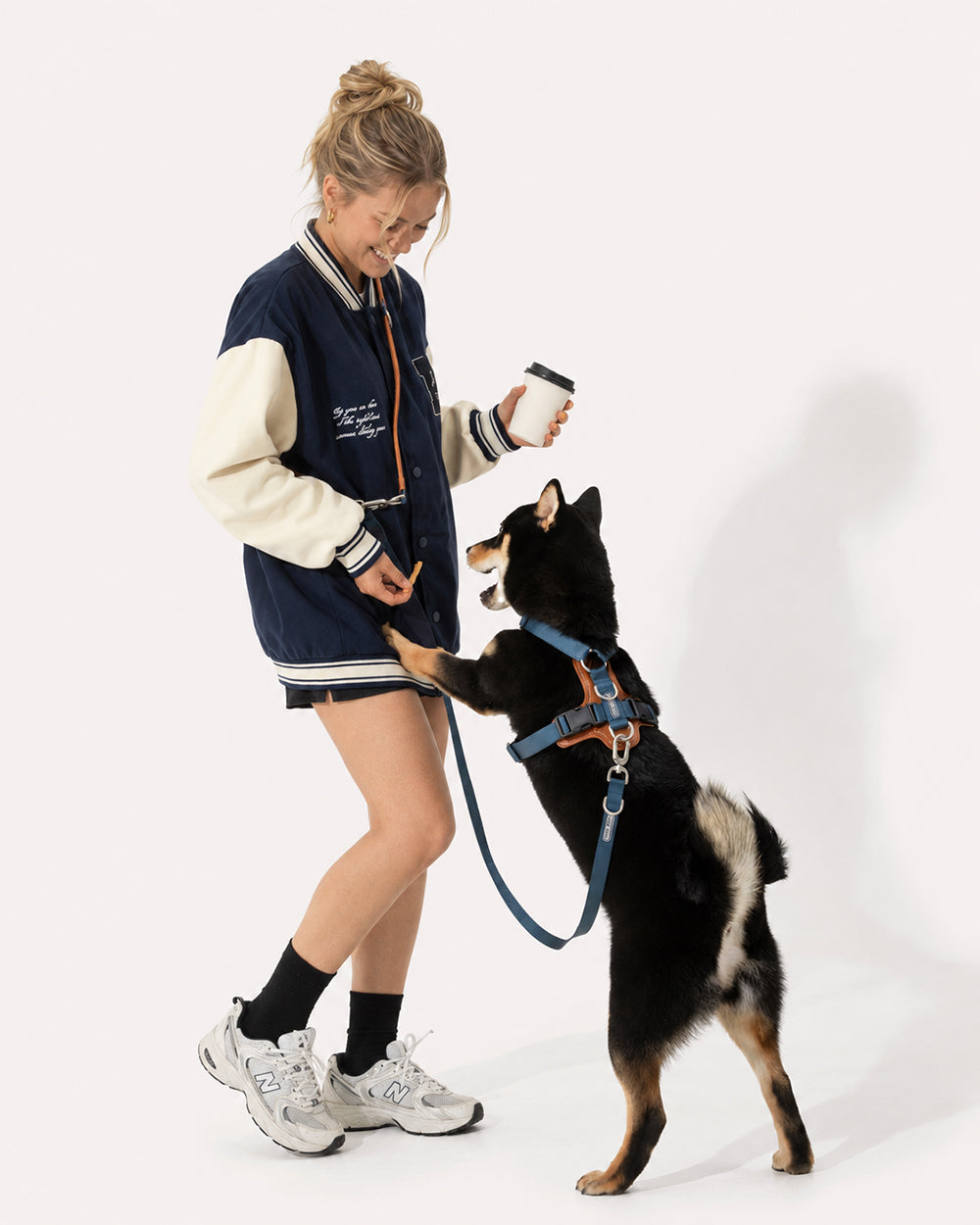 A dog in a navy blue step-in harness, with the owner using a crossbody leash and pouch, freeing hands to interact.
