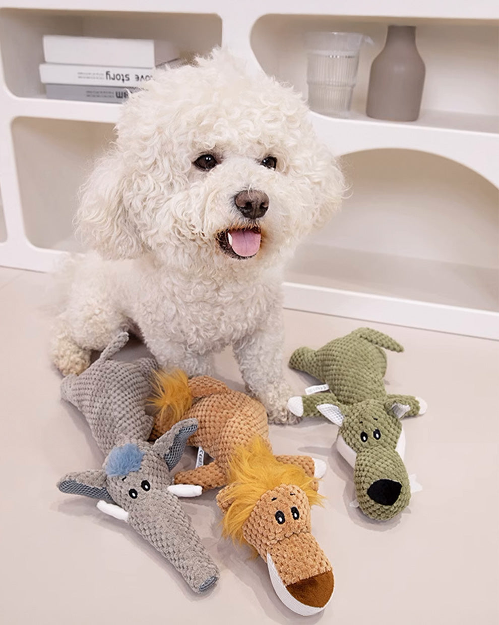 A small white dog sitting next to three plush squeaky toys.